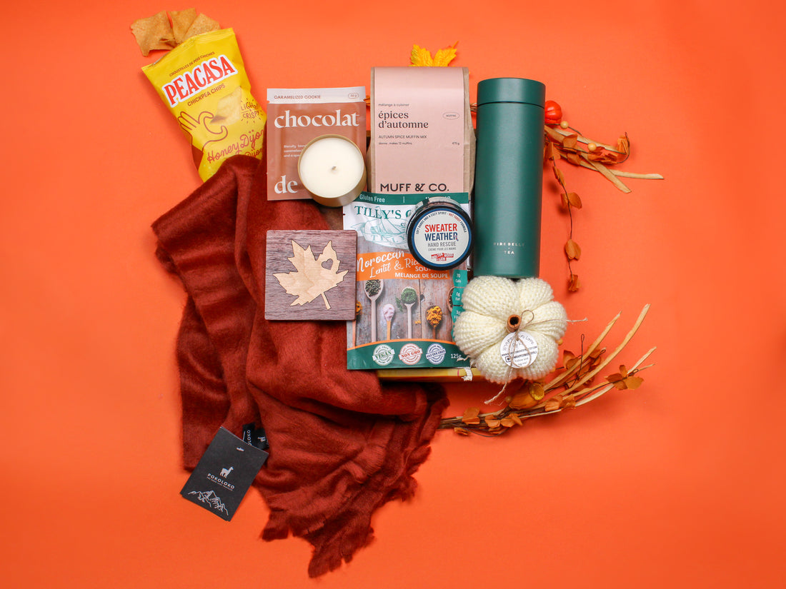 Fall Cozy Box flat lay with Canadian-made autumn treats and cozy essentials—scarf, tea tumbler, pumpkin spice mix, candle, chocolate, and seasonal snacks—styled with warm fall tones.